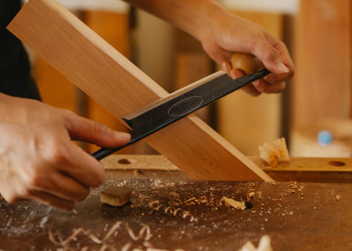 Male artisan shaping plank with drawknife